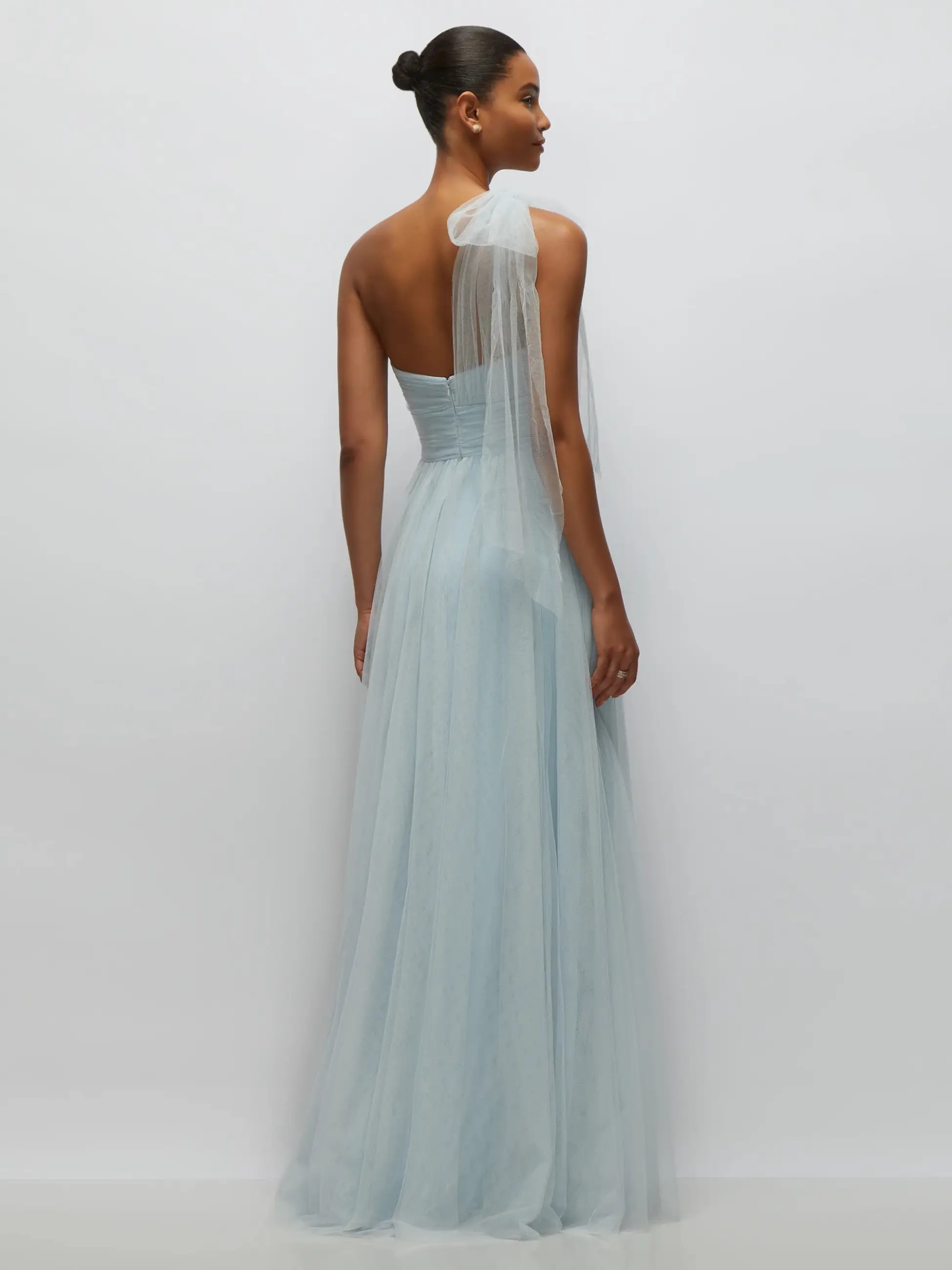 Model is wearing a one shoulder gown with sweetheart neckline, tulle bow on the shoulder, and a floor length tulle skirt