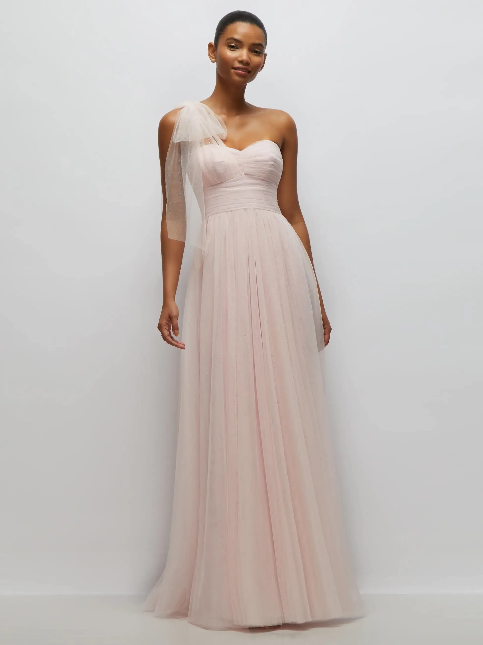 Model is wearing a one shoulder gown with sweetheart neckline, tulle bow on the shoulder, and a floor length tulle skirt