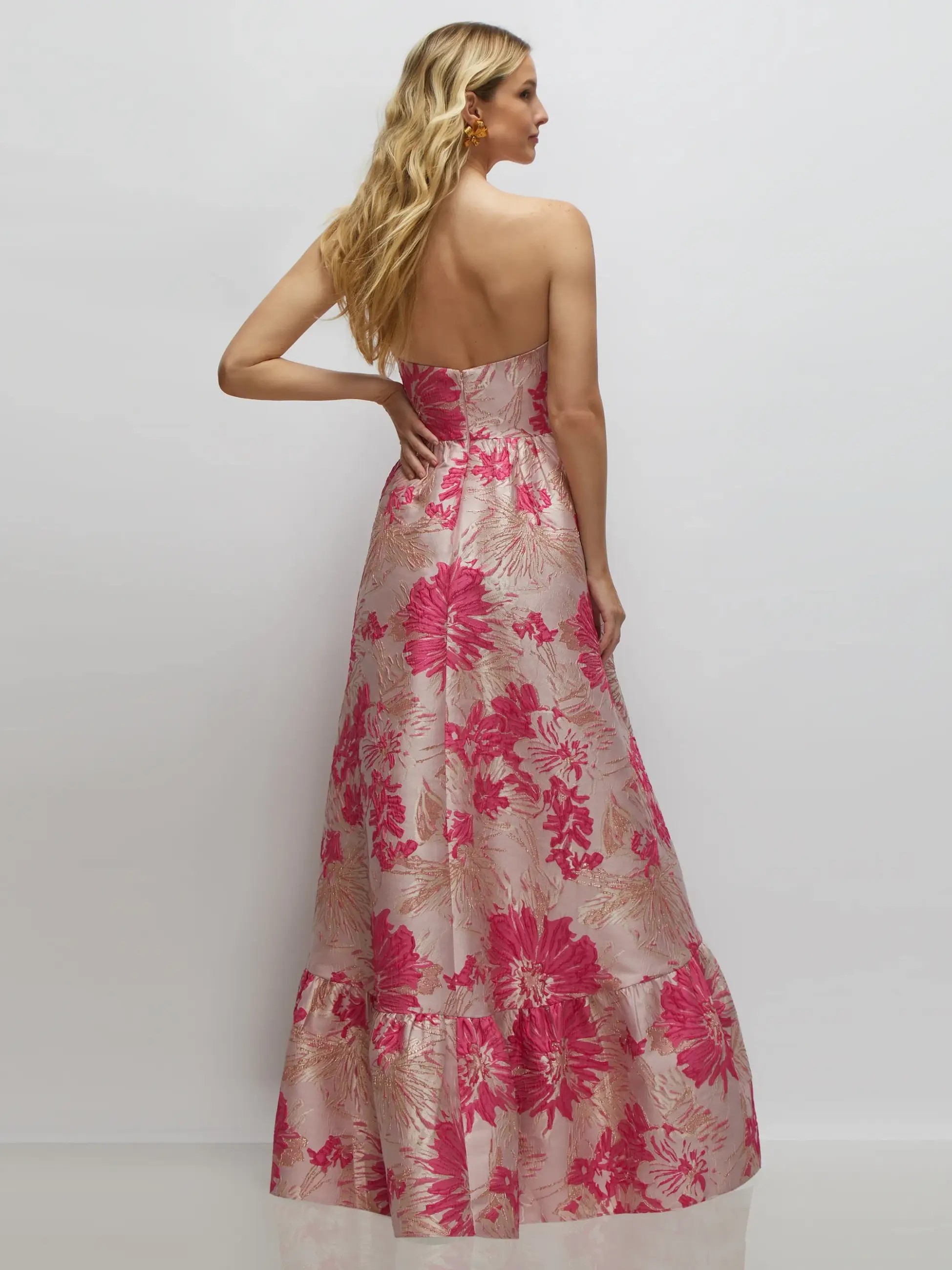 Model is wearing a strapless pink floral floor length gown with a large ruffle at the bottom