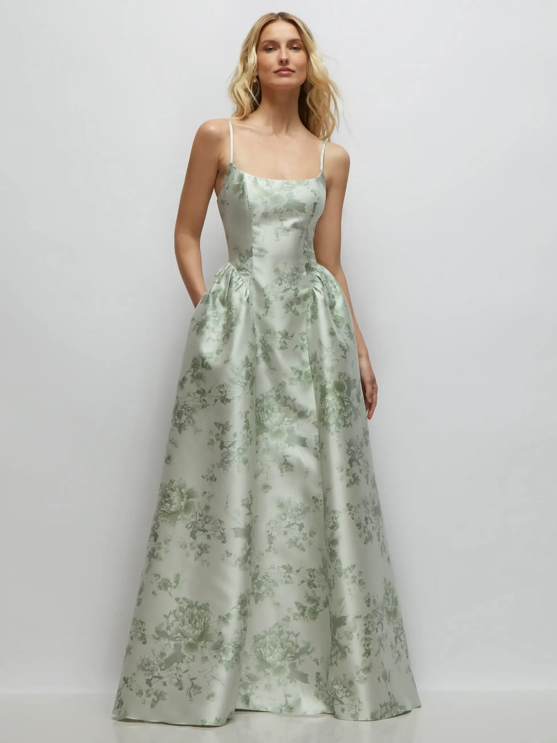 A model wearing a light green floral satin gown with thin straps and pockets.