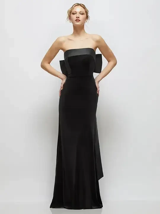 A model wearing a strapless black gown with a bow detail at the back, standing against a plain background.