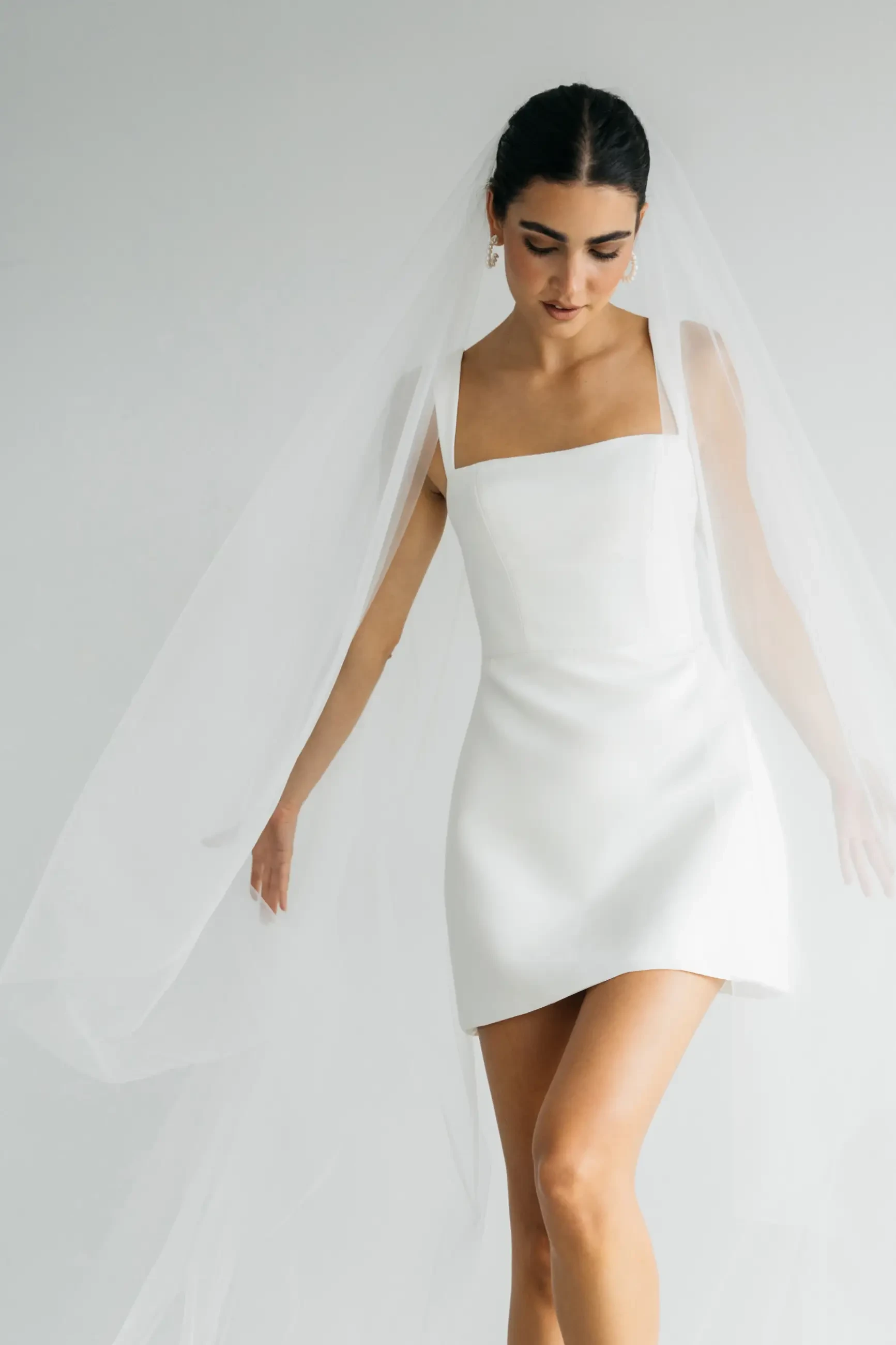 Model is a sleeveless mini wedding dress made of smooth fabric