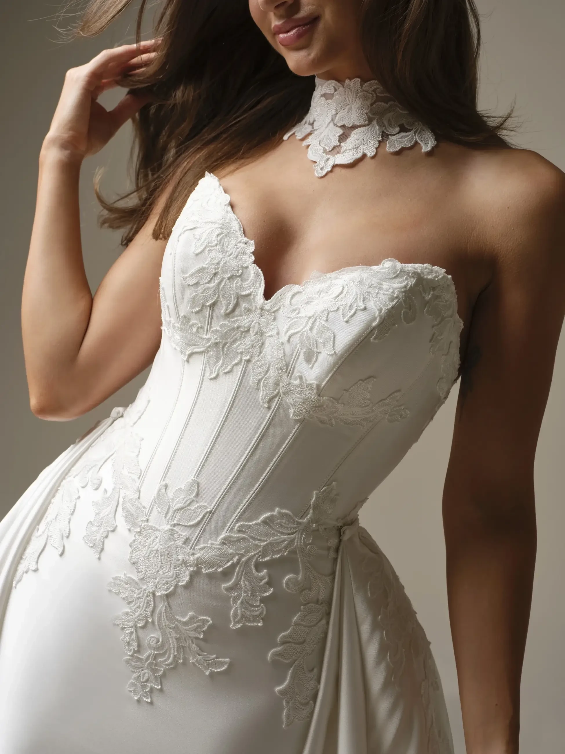 A woman wearing a white bridal gown with intricate lace detailing on the bodice and a matching choker.