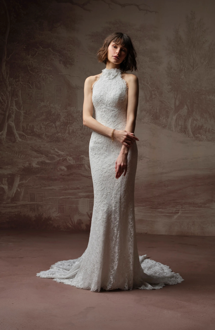 A model wearing an elegant white lace wedding dress with a high neckline, standing gracefully against a textured background.