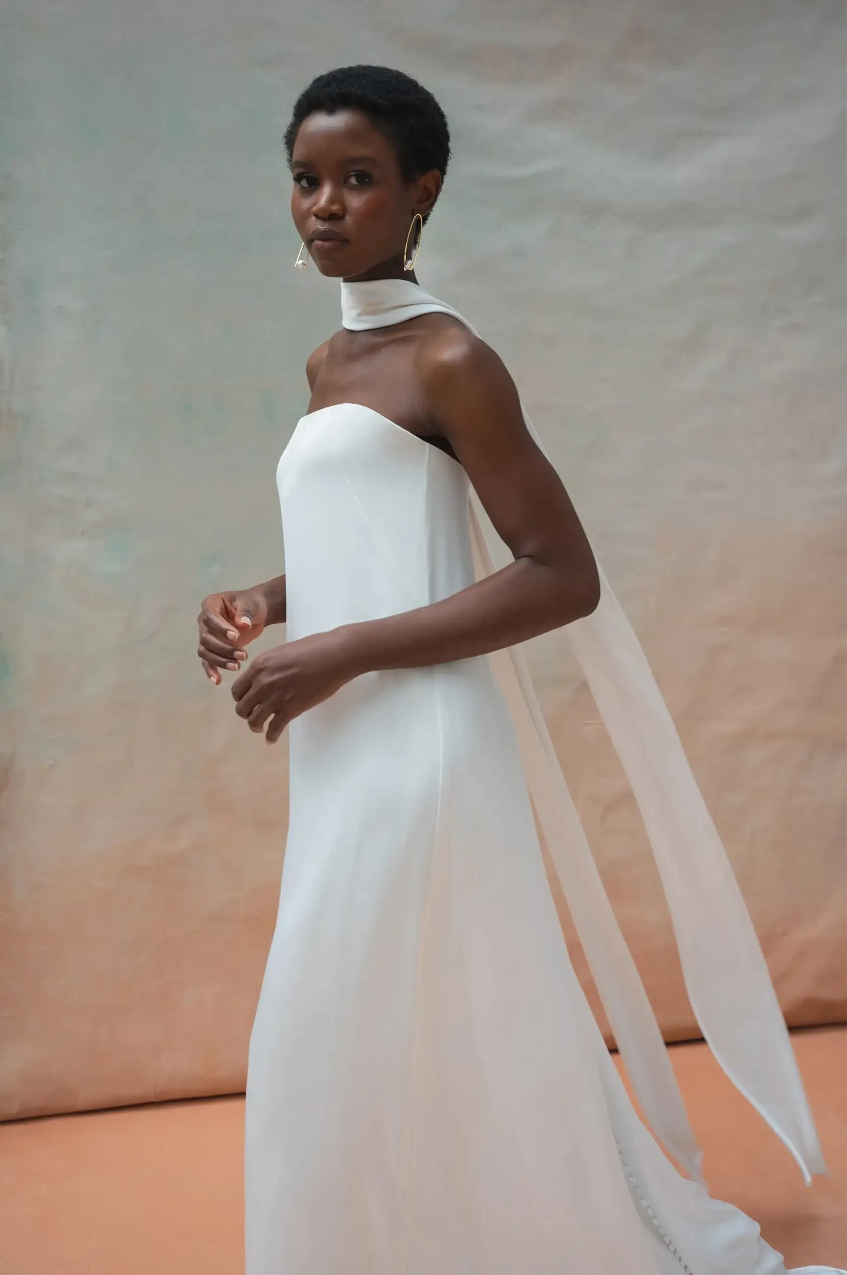 Model is wearing a strapless minimalist loose wedding dress with a bridal neck scarf draped around her neck