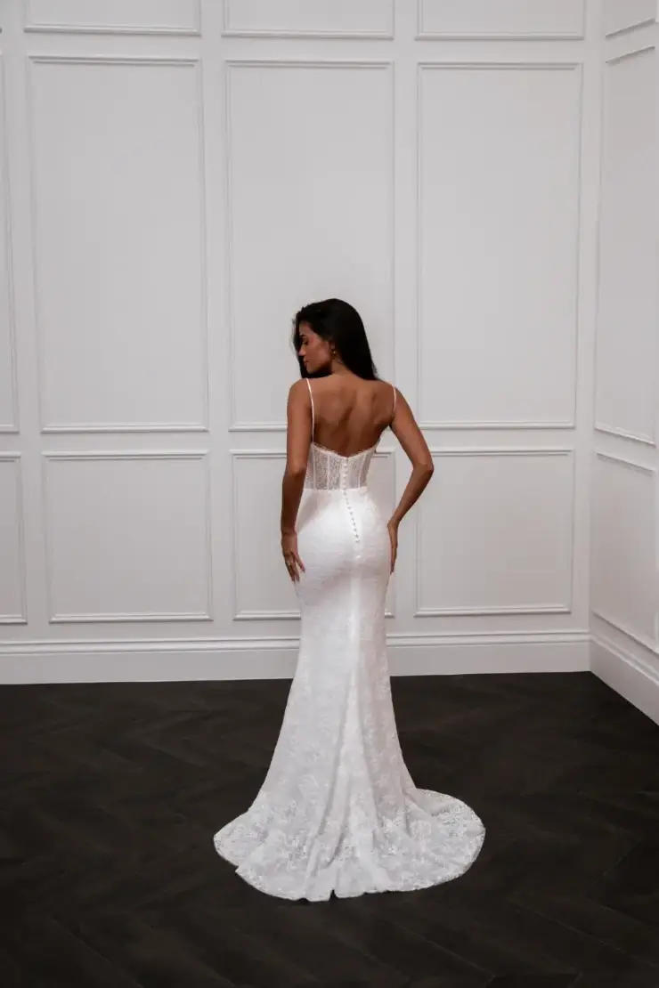 Model is wearing a sleeveless fit and flare wedding dress with a corset bodice and spaghetti straps