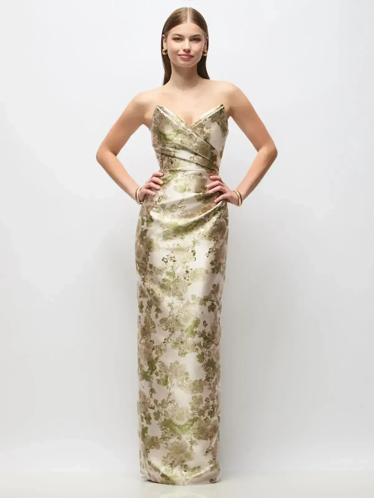 A woman wearing a strapless, floor-length gown with a floral design in shades of gold and cream.