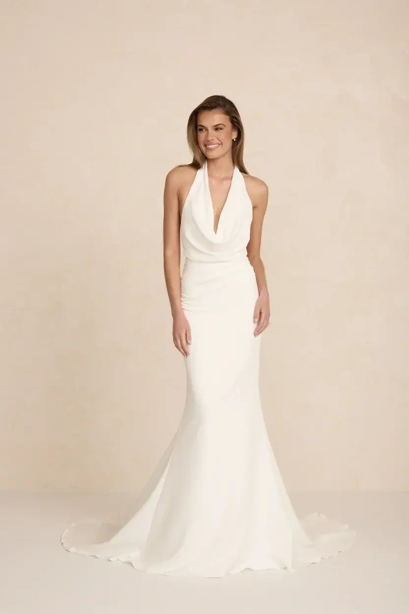 A woman in a white halter neck gown with a fitted silhouette, smiling against a neutral background.
